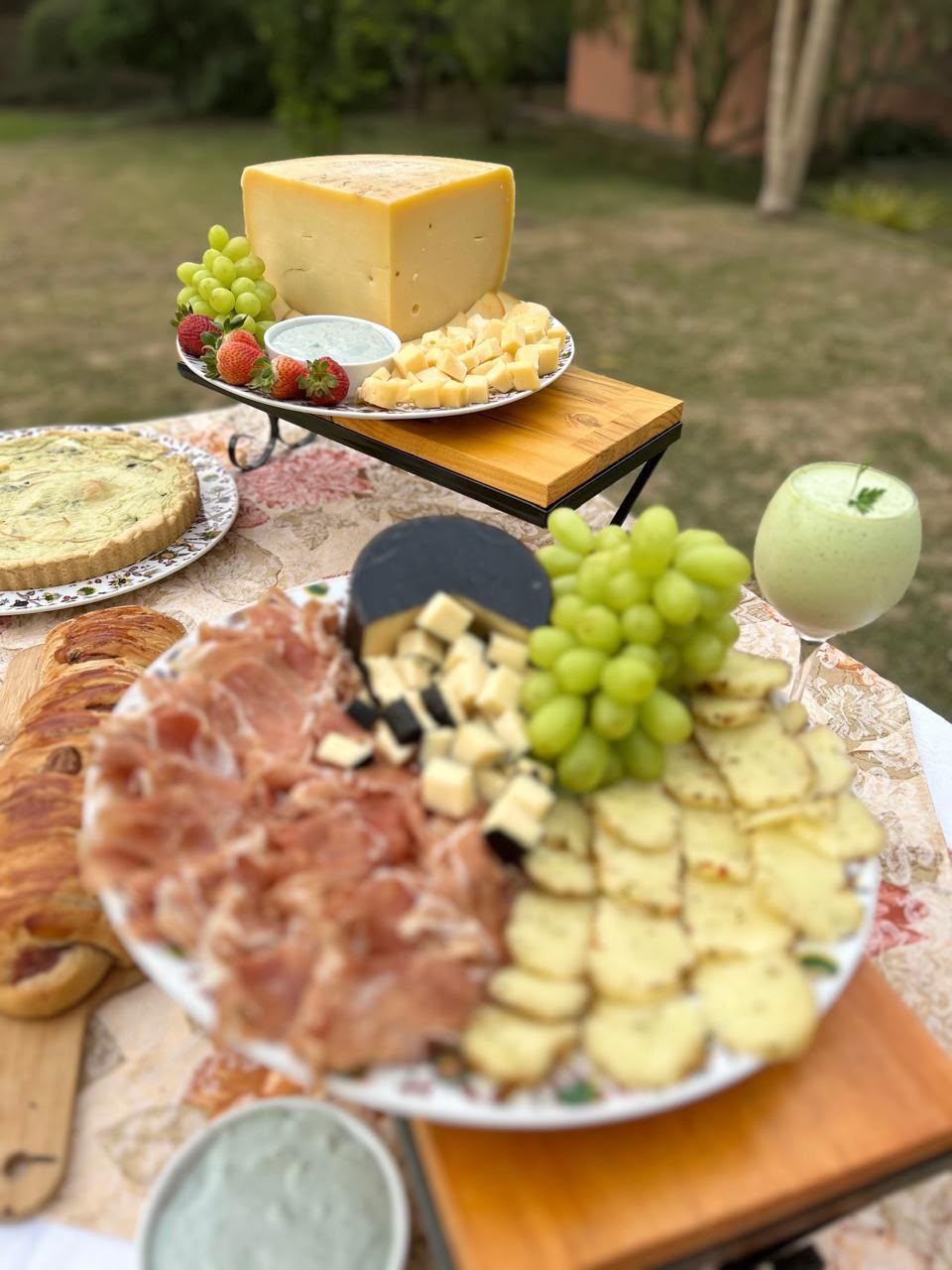 Mesa com tábua de queijos, frios e uvas ao ar livre